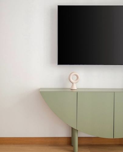 Sage green curved sideboard below a mounted TV with a ring-shaped ceramic sculpture