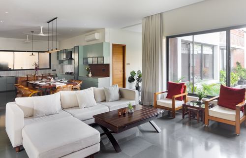 Open-plan living room with white sectional, wooden armchairs, and glass wall opening to courtyard