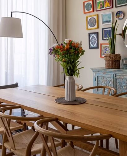 Wooden dining table with wishbone chairs, floral centerpiece, arc lamp, and colorful gallery wall behind