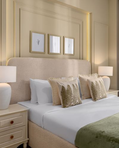 Beige upholstered bed with fern-embroidered pillows beneath framed art and paneled wall.