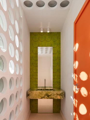 Narrow powder room with green tiled vanity, perforated pink tile wall, and orange door with light patterns