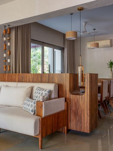 Living room with fluted teak partition, beige sofa and brass pendant lights beside dining area