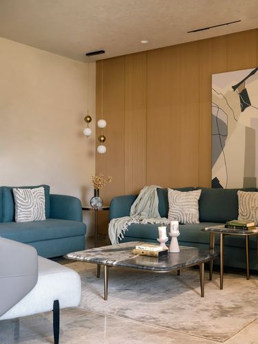 Living room with teal sofas, marble coffee table, and fluted wood wall with brass pendant lights