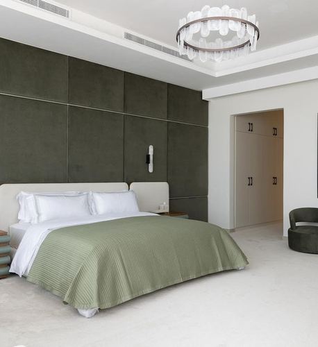 Bedroom with olive velvet paneled wall, white bed, sage throw, and round crystal chandelier