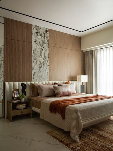 Bedroom with fluted wood and stone panel wall behind a cream channel-tufted bed with rust throw