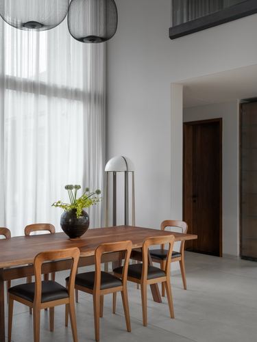 Wood dining table with leather chairs beneath woven pendant lights against a sheer curtained wall