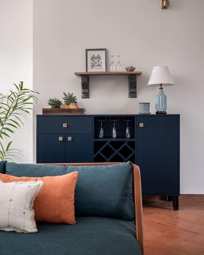 Navy blue bar cabinet with wine rack below a wooden shelf, teal sofa with orange cushions in front