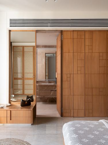 Wooden panelled wardrobe beside open door revealing marble-clad bathroom in warm-toned bedroom