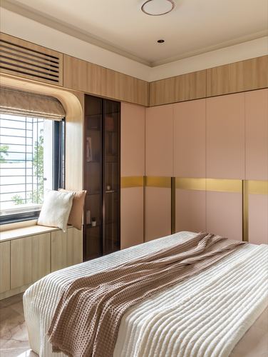 Pink and wood bedroom with wardrobe wall, brass trim, and a window seat beside the bed