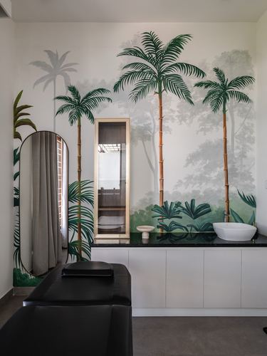 Bathroom vanity with vessel sink and black countertop against a painted tropical palm mural