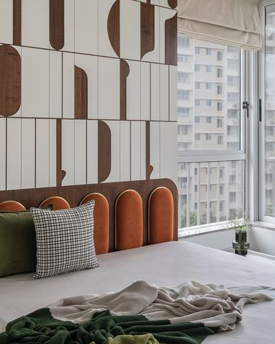 Bedroom with sculptural wood-paneled wall, arched orange leather headboard, and city-view window