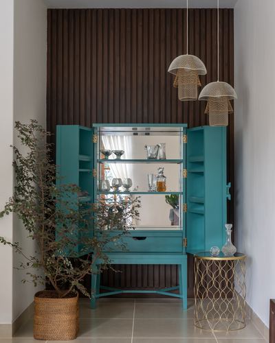 Teal mirrored bar cabinet open against ribbed dark wood wall with woven pendant lights
