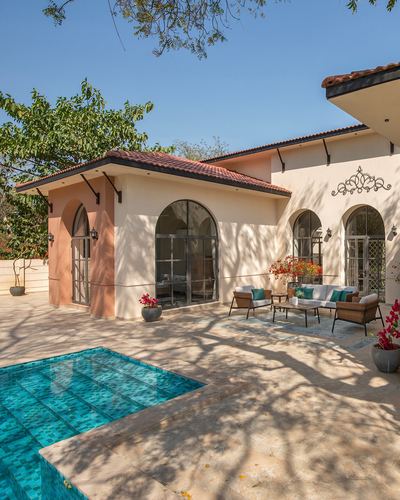 Villa facade with arched windows, terracotta roof, and teal-tiled pool under trees