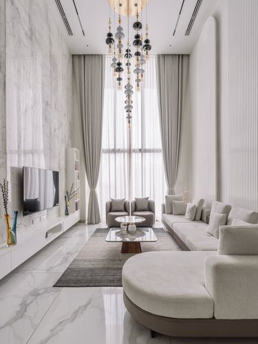 Double-height living room with marble wall, tall sheer curtains, cascading glass-bead chandelier, and neutral sectional seating.