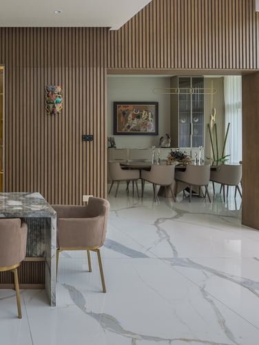 Marble-floored dining area seen through fluted wood archway with beige chairs and framed art