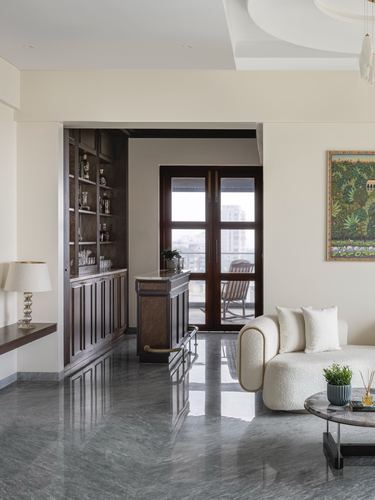 Living room with grey marble floor, cream sofa, and dark wood bar niche framed by an archway