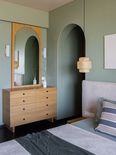 Sage green bedroom with arched mirror, wooden dresser, and woven pendant light beside bed