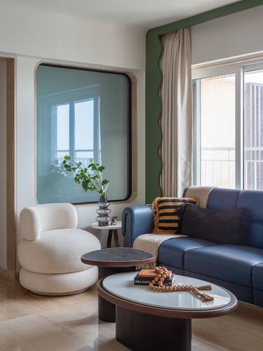 Living room corner with navy leather sofa, cream bouclé chair, and round nested coffee tables under a scalloped mirror