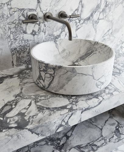 Round marble vessel sink on veined marble countertop with brushed metal wall-mounted faucet