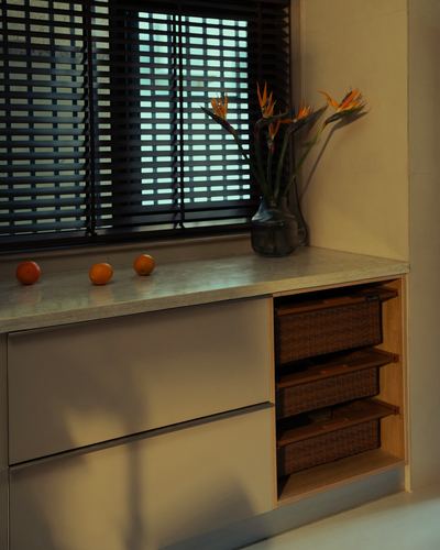 Kitchen counter corner with venetian blinds, flowers, oranges, and woven basket drawers