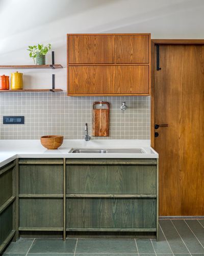 Kitchen corner with green wood cabinets, teak upper cabinet, tiled backsplash, and sliding wood door