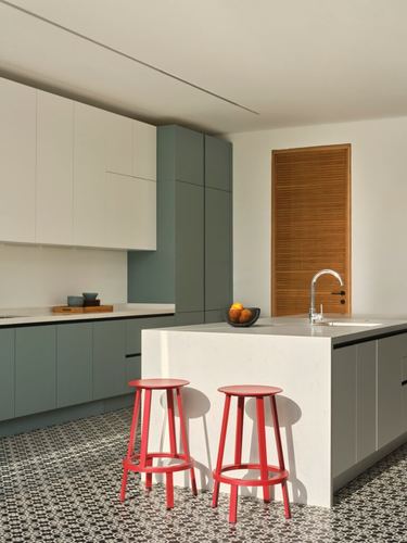 Modern kitchen with green cabinetry, white island, red stools and patterned tile floor.