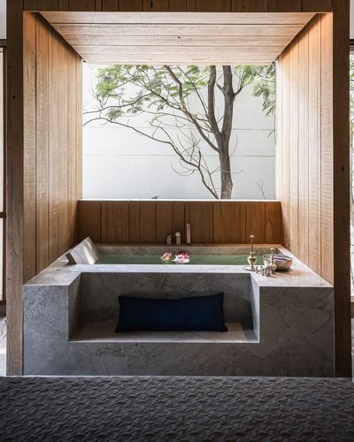 Sunken stone bathtub framed by wood paneling facing a window view of a tree