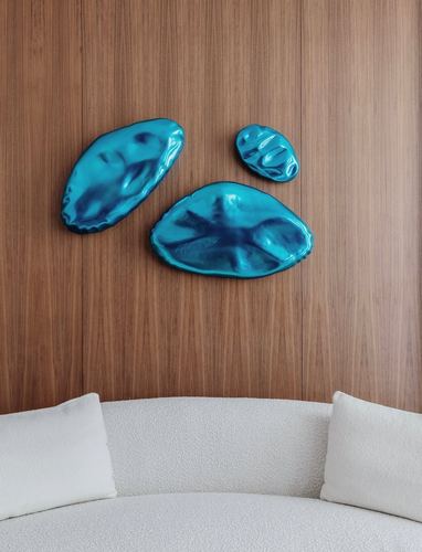 Three glossy blue organic wall sculptures on wood paneling above a white bouclé sofa
