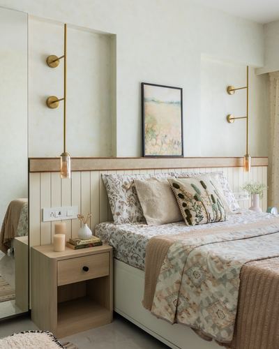 Pastel bedroom with wood-panelled headboard wall, brass sconces, and floral bedding