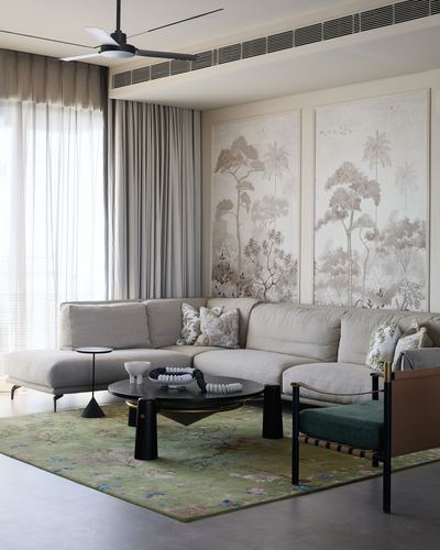 Beige sectional sofa beneath two large botanical wall panels, green patterned rug, black coffee table
