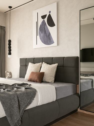 Grey tufted bed with cream and rust pillows beneath abstract art on a textured wall.