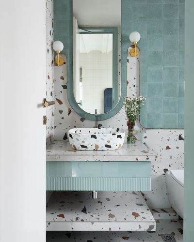 Sage green bathroom with terrazzo sink, arched mirror, and brass globe sconces