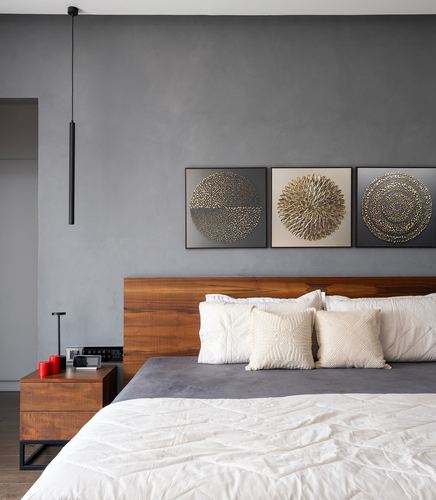 Bedroom with wood headboard, grey textured wall, three round artworks, and a slim black pendant light