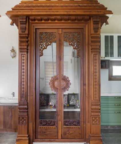 Intricately carved wooden pooja unit with glass doors and deity idols inside a modern home