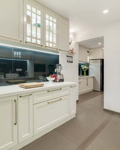 Cream galley kitchen with white countertop, black backsplash, and glimpse into inner kitchen with fridge