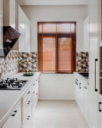 White galley kitchen with patterned triangle backsplash and wooden blinds on end window