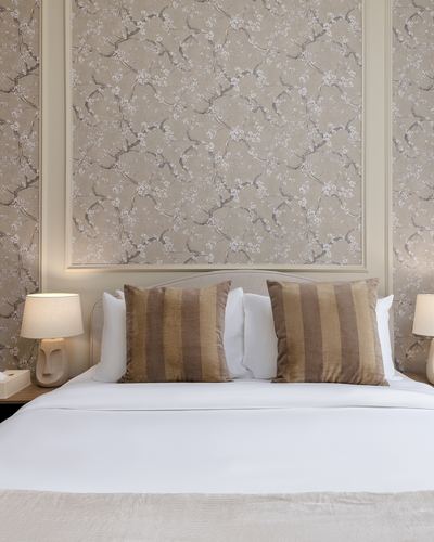 Bed with striped cushions beneath a floral wallpaper panel flanked by table lamps