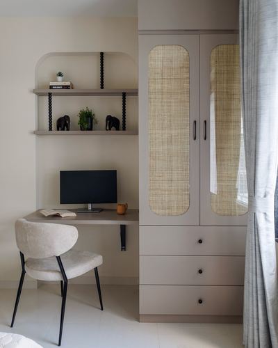 Beige study nook with cane-front wardrobe, wall-mounted desk, monitor and upholstered chair