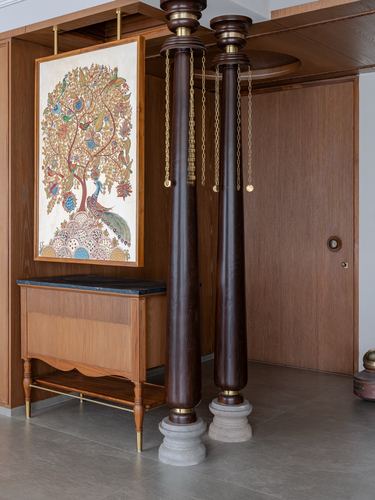 Foyer with two dark wood turned columns hung with brass chains beside a folk-art painting