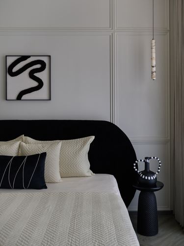 Bedroom corner with black curved headboard, cream pillows, abstract art and marble pendant light.