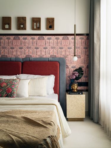 Bedroom with red and grey headboard, pink patterned wallpaper, and mosaic bedside table with brass buddha