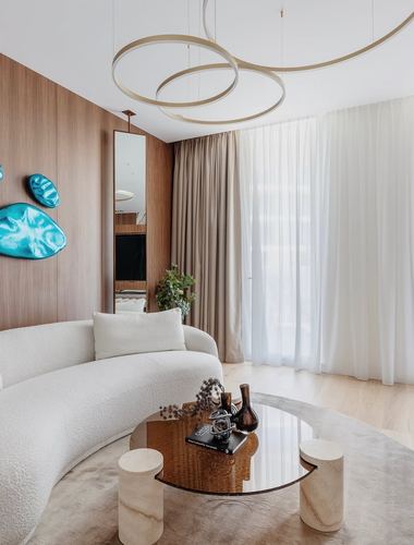 Curved white sofa and round glass table in a wood-paneled living room with sheer curtains