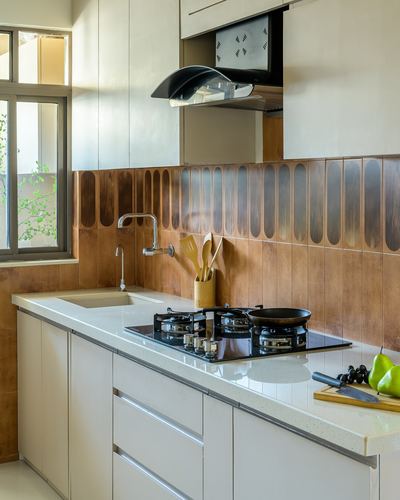 Modern kitchen counter with black hob, wood-patterned scalloped backsplash and white cabinetry