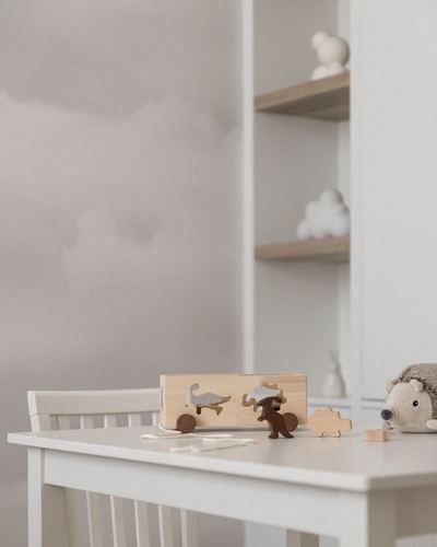 White child's desk with wooden animal toys, cloud-patterned wall, shelf with plush decor behind