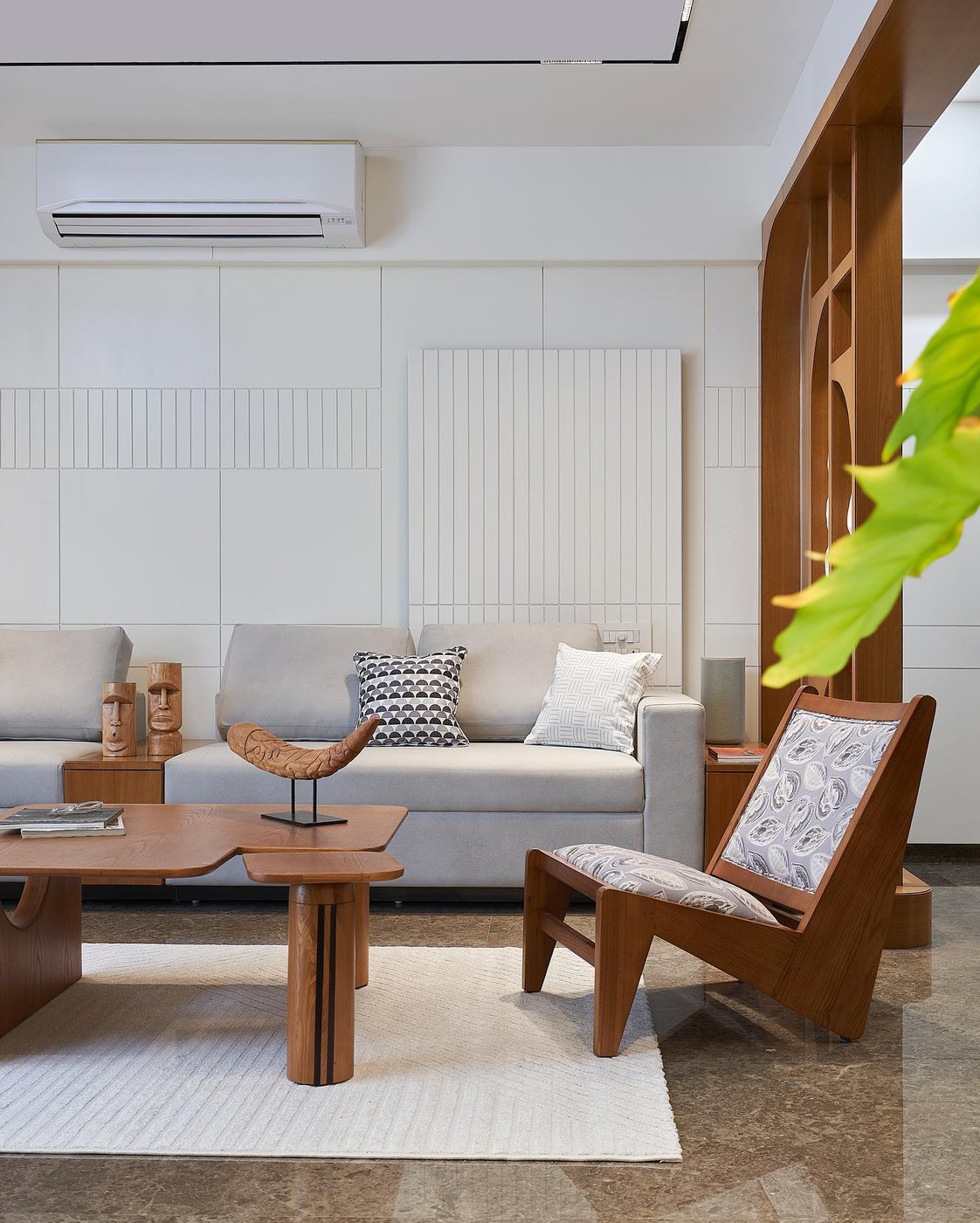 Living room with grey sofa, teak lounge chair, carved wood partition and marble floor