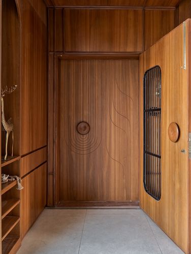 Entryway with carved wooden door and open door showing black metal grille, stone floor