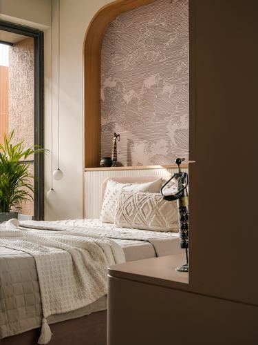 Bedroom with arched wooden niche, patterned wallpaper, pendant lights and textured white bedding