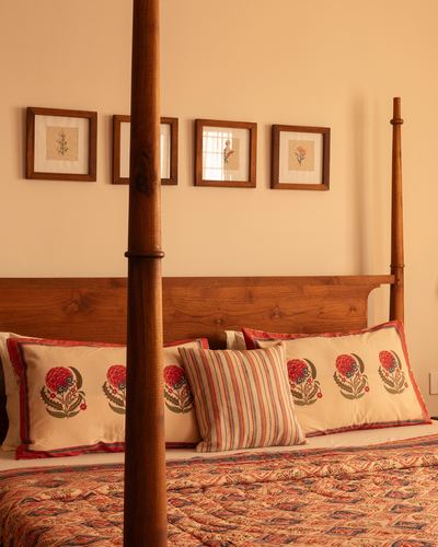 Wooden four-poster bed with embroidered floral pillows against peach wall with framed art