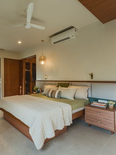 Bedroom with walnut bed, olive linens, brass sconces and a hanging pendant light