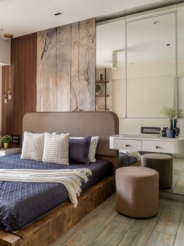 Bedroom with stone-paneled headboard wall, navy bedding, wooden platform bed, and mirrored vanity nook